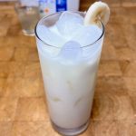 Banana milk in a glass with a slice of banana on the rim.