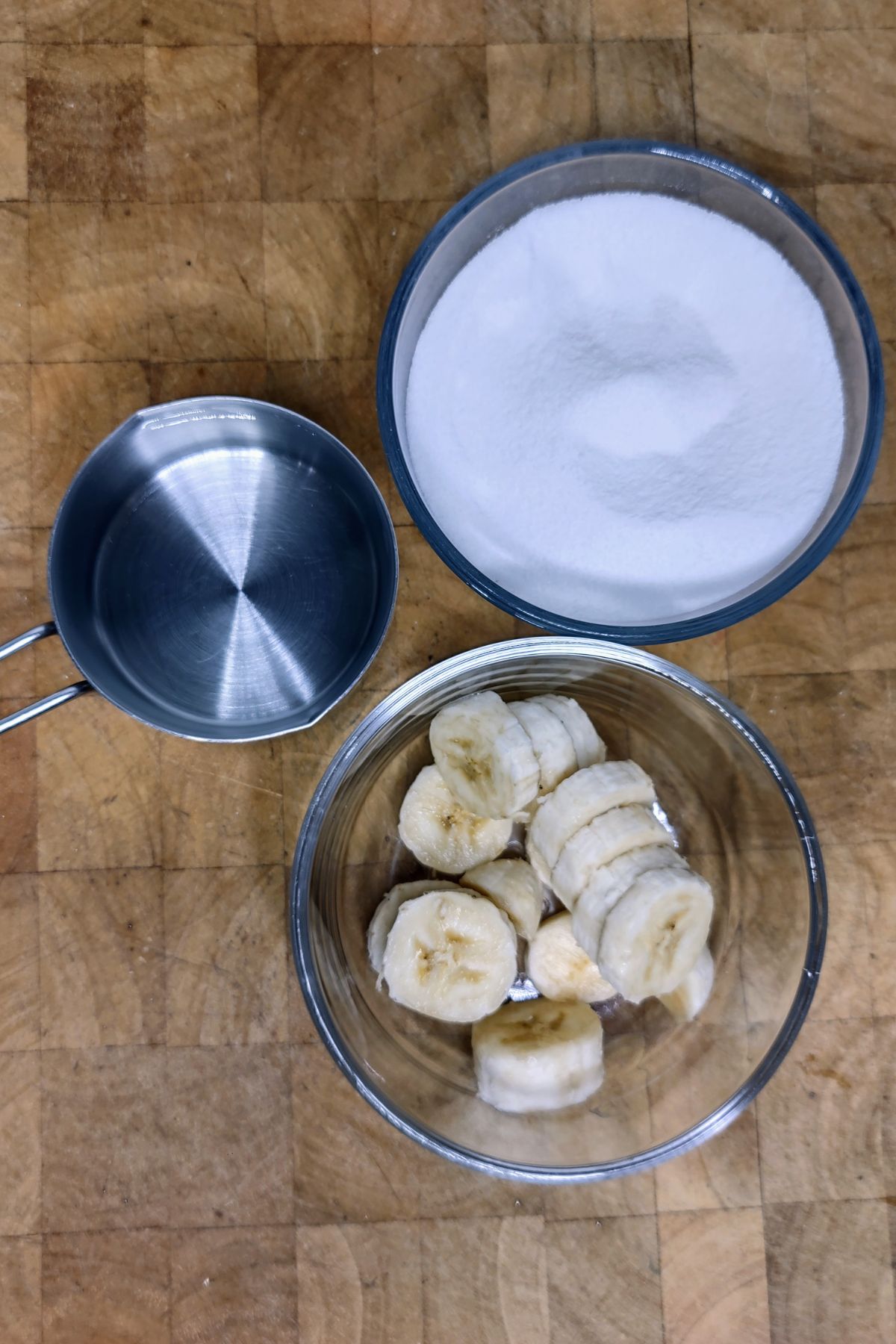 Bowls of banana, sugar and water on a wooden table.