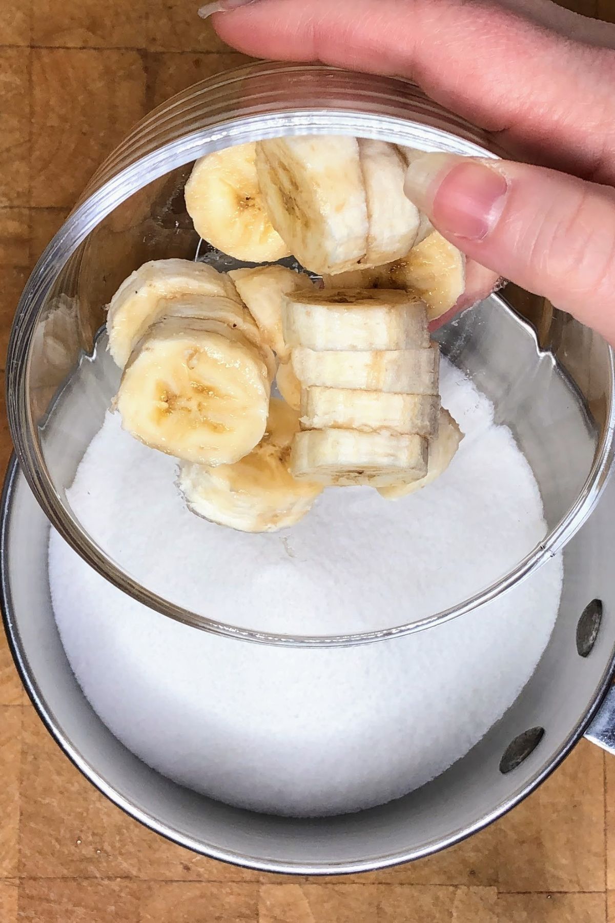 Pouring bananas into a pot with sugar.
