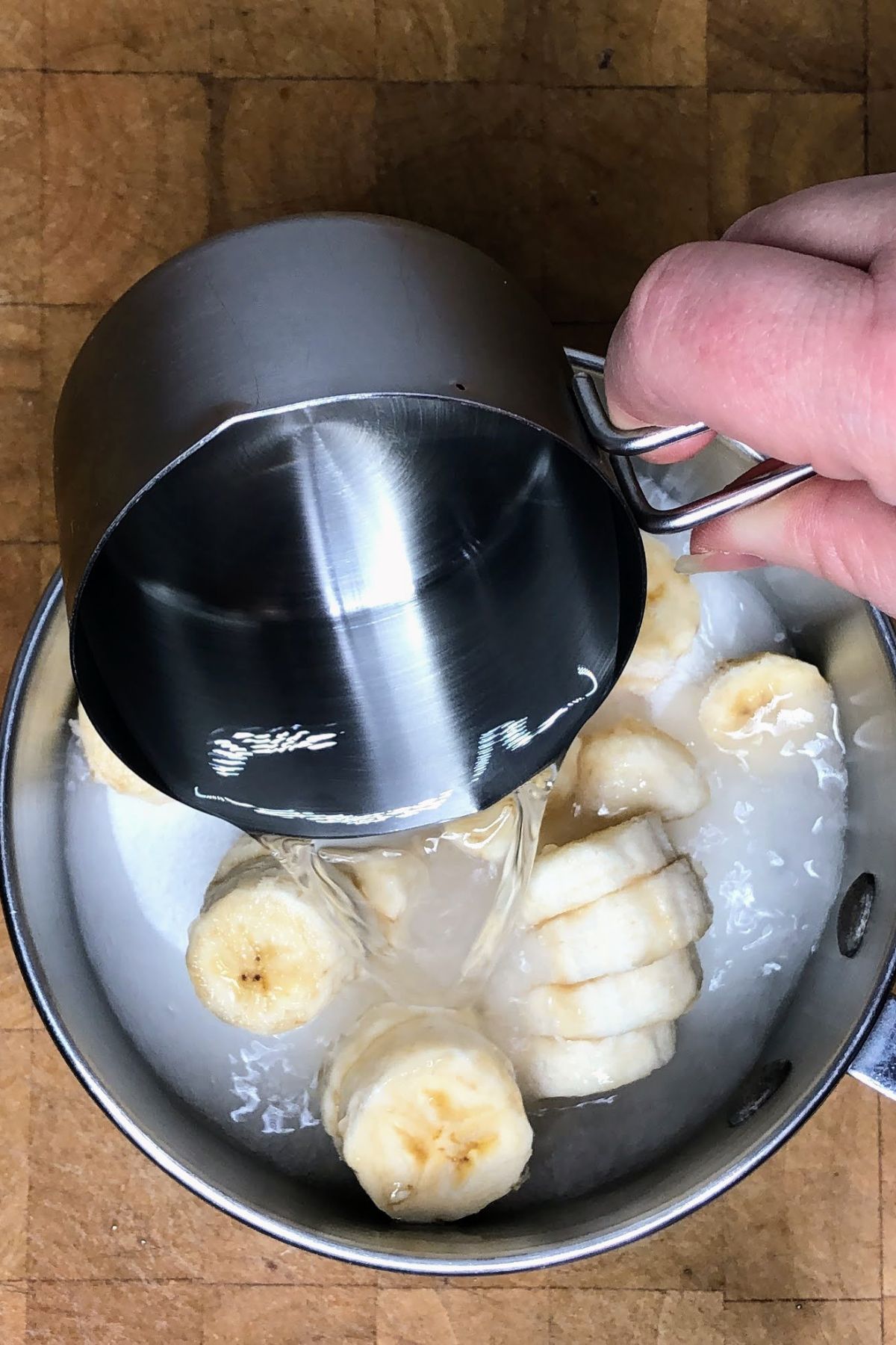 Pouring water into a pot with banana slices.