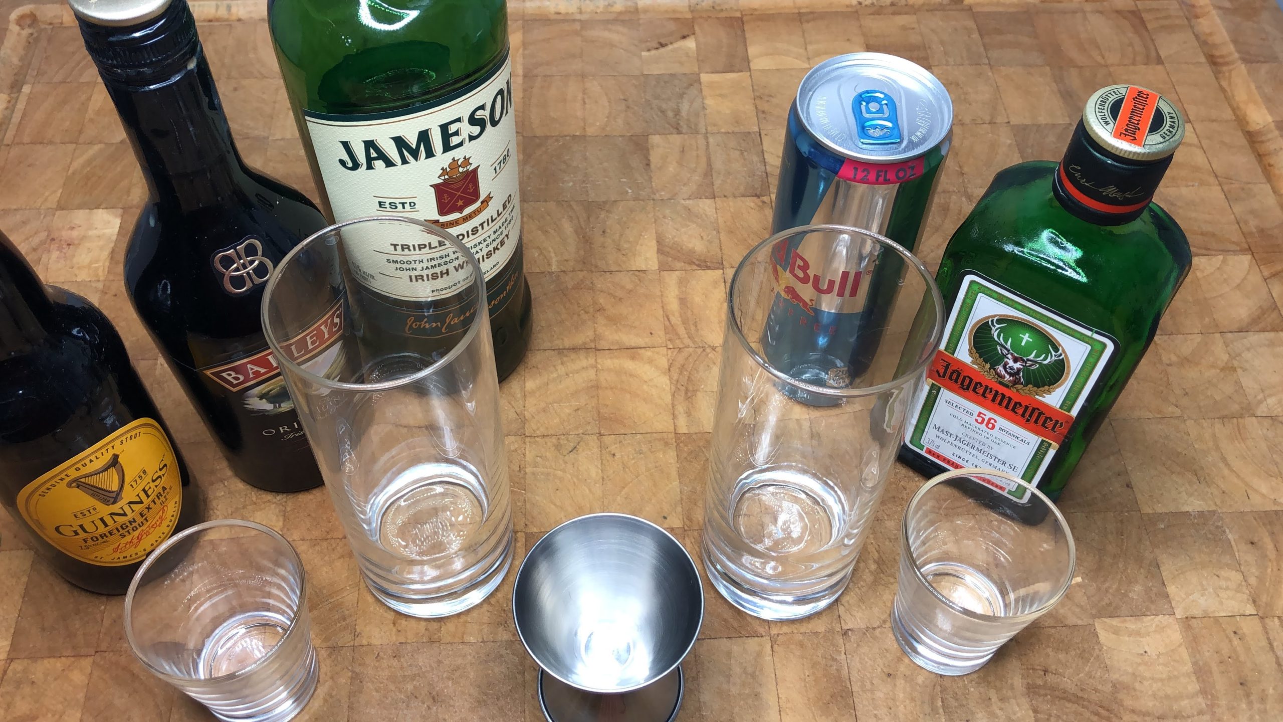 Guiness, Irish Cream, Jameson's, red bull and jager next to a jigger, two shot glass and two highball glasses.