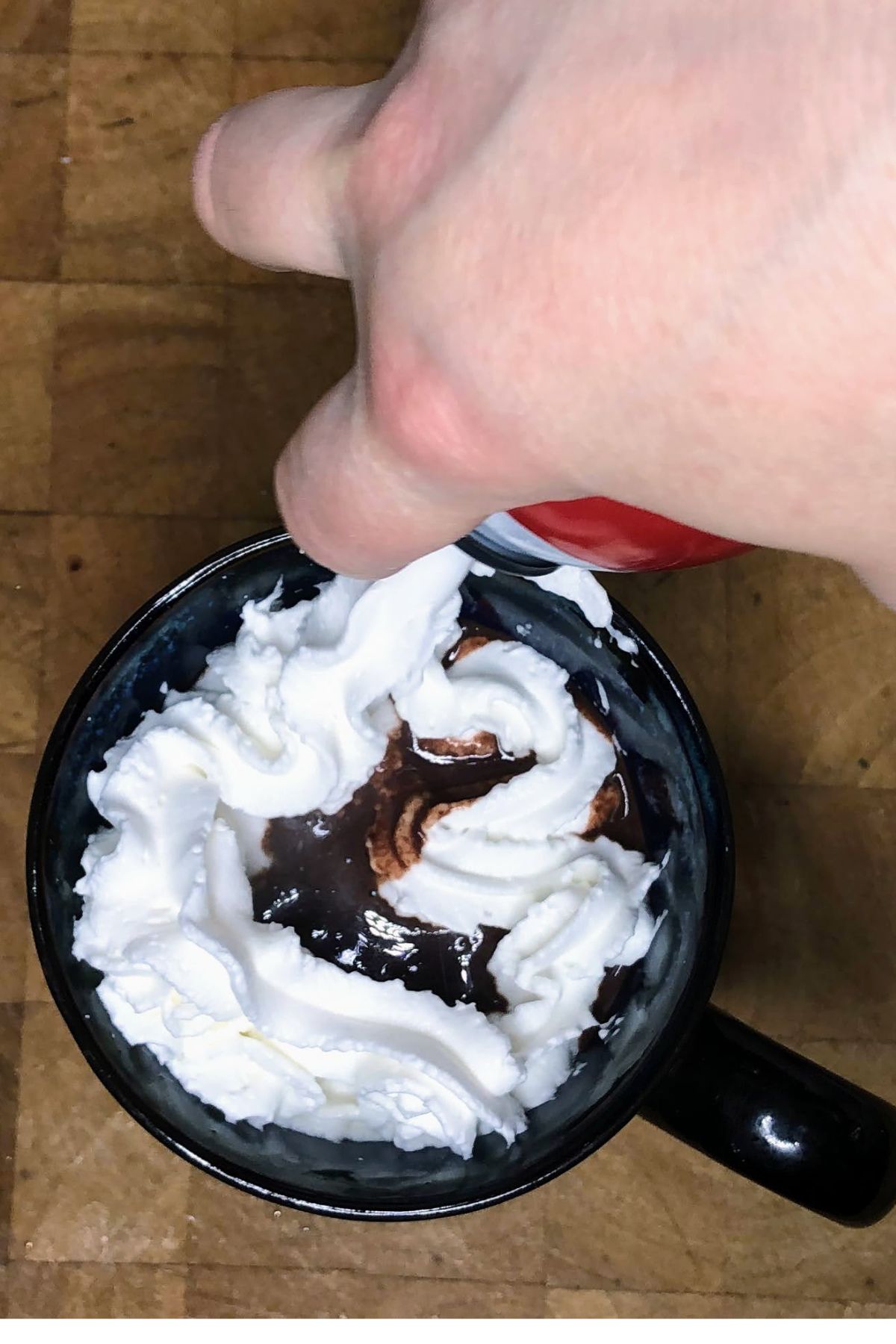 Putting whipped cream on top of biscoff hot chocolate.