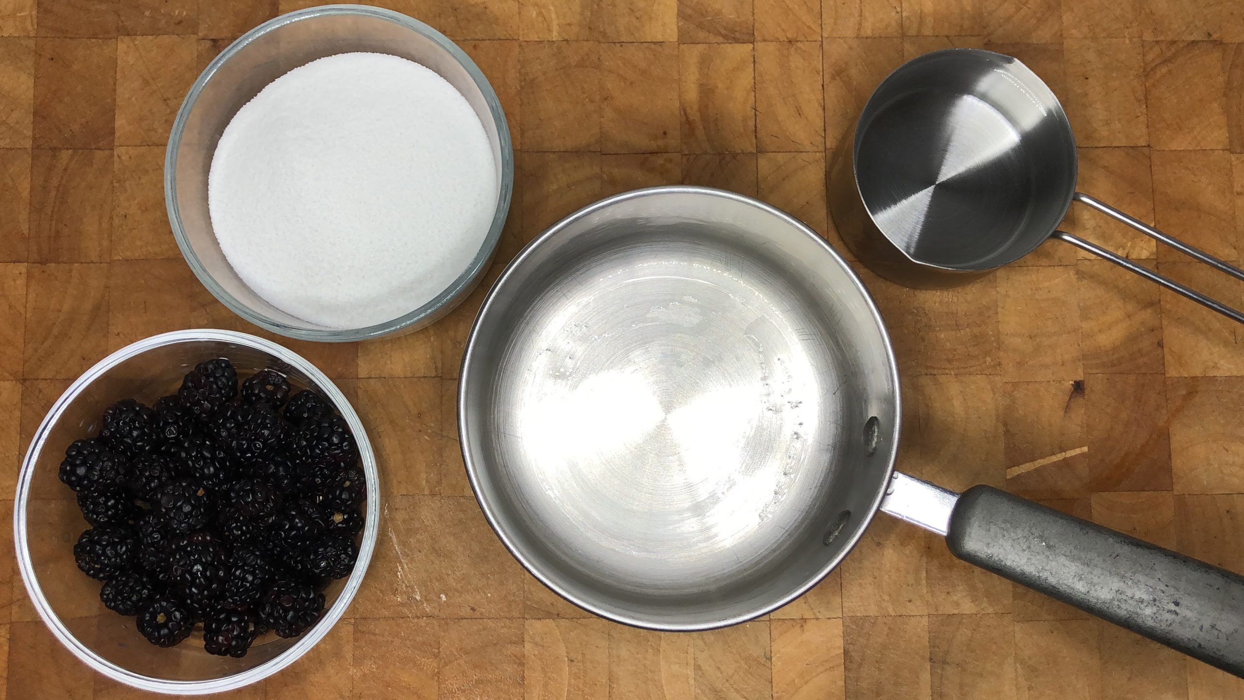 Bowls of sugar, water and blackberries next to an empty pot.