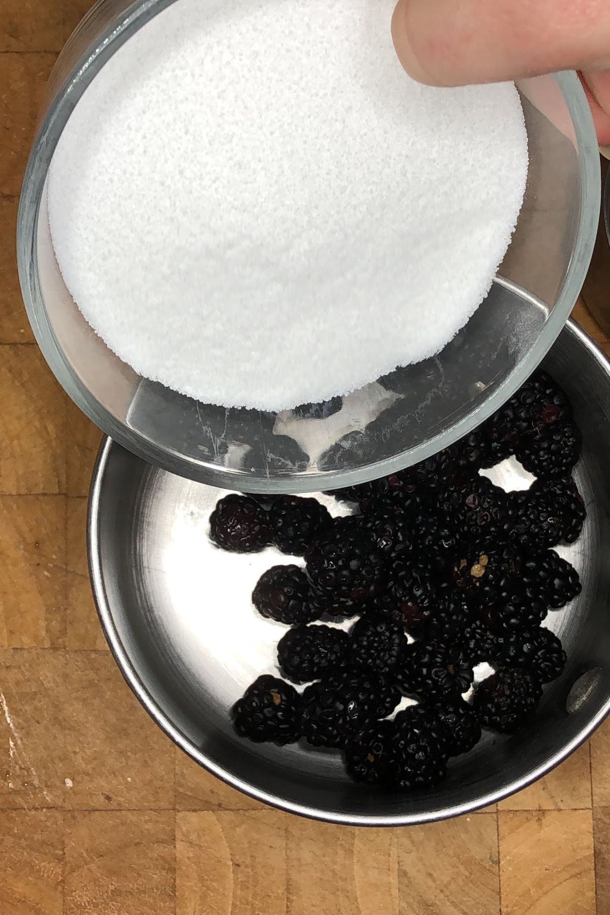 Pouring sugar into a pot with blackberries.