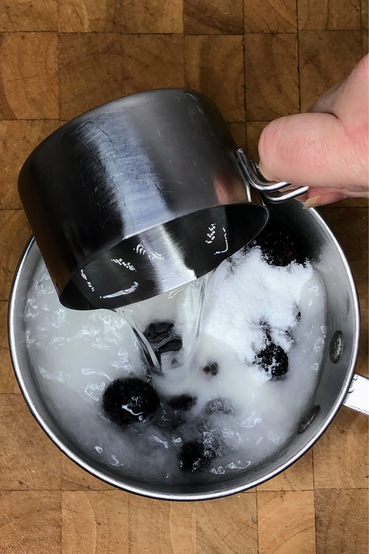 Pouring water into a pot with sugar and blackberries.