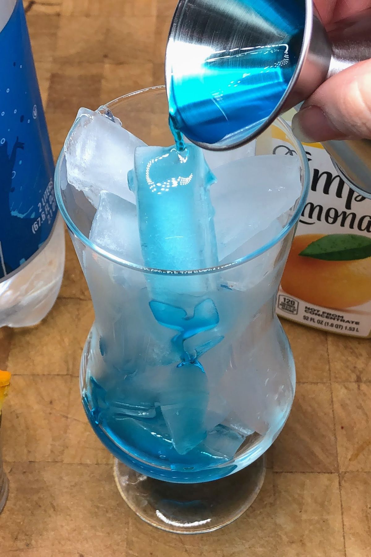 Pouring blue curacao from a jigger into a hurricane glass.