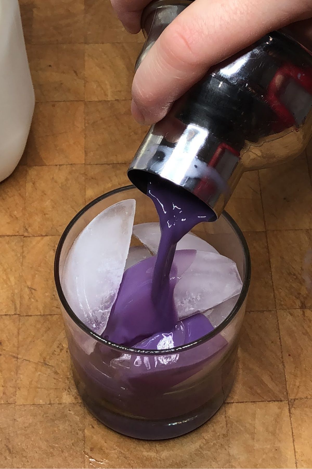 Pouring blueberry milk from a cocktail shaker into a rocks glass.