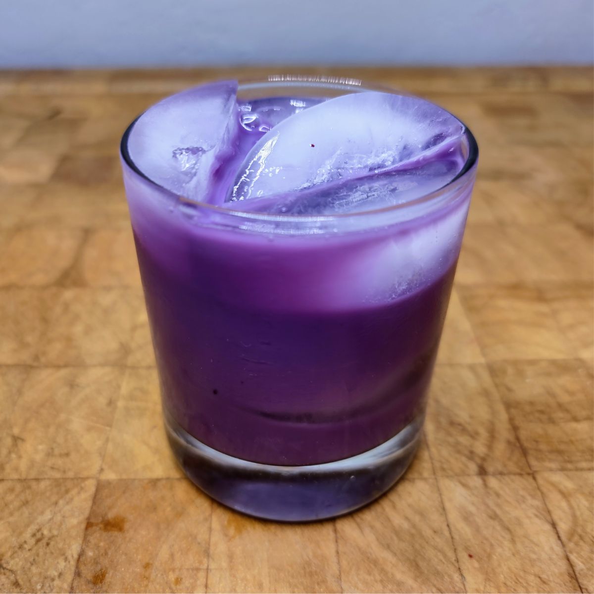 Blueberry milk in a rocks glass on a wooden table.
