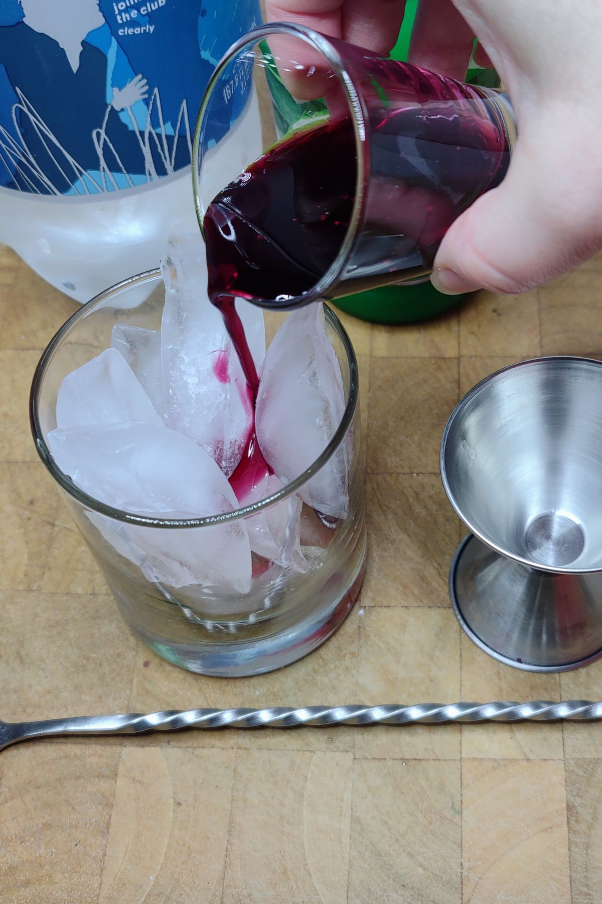 Pouring blueberry simple syrup into a rocks glass.