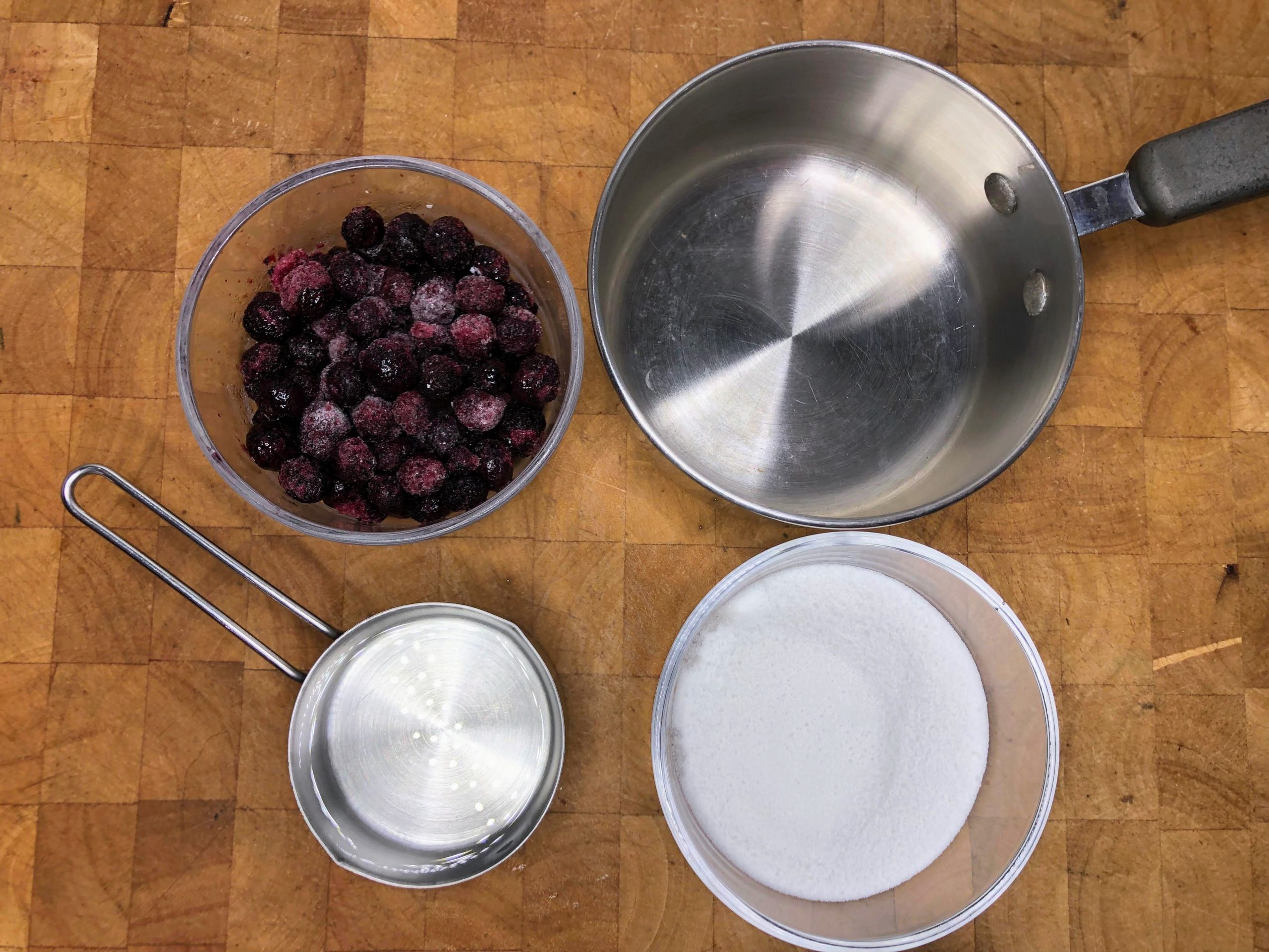 Bowl of blueberries, water and sugar next to a saucepan