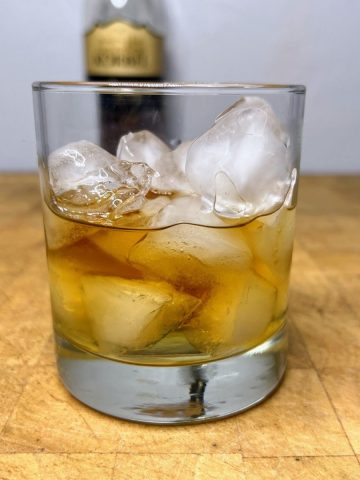 Brandy on the rocks in a glass on a wooden table.