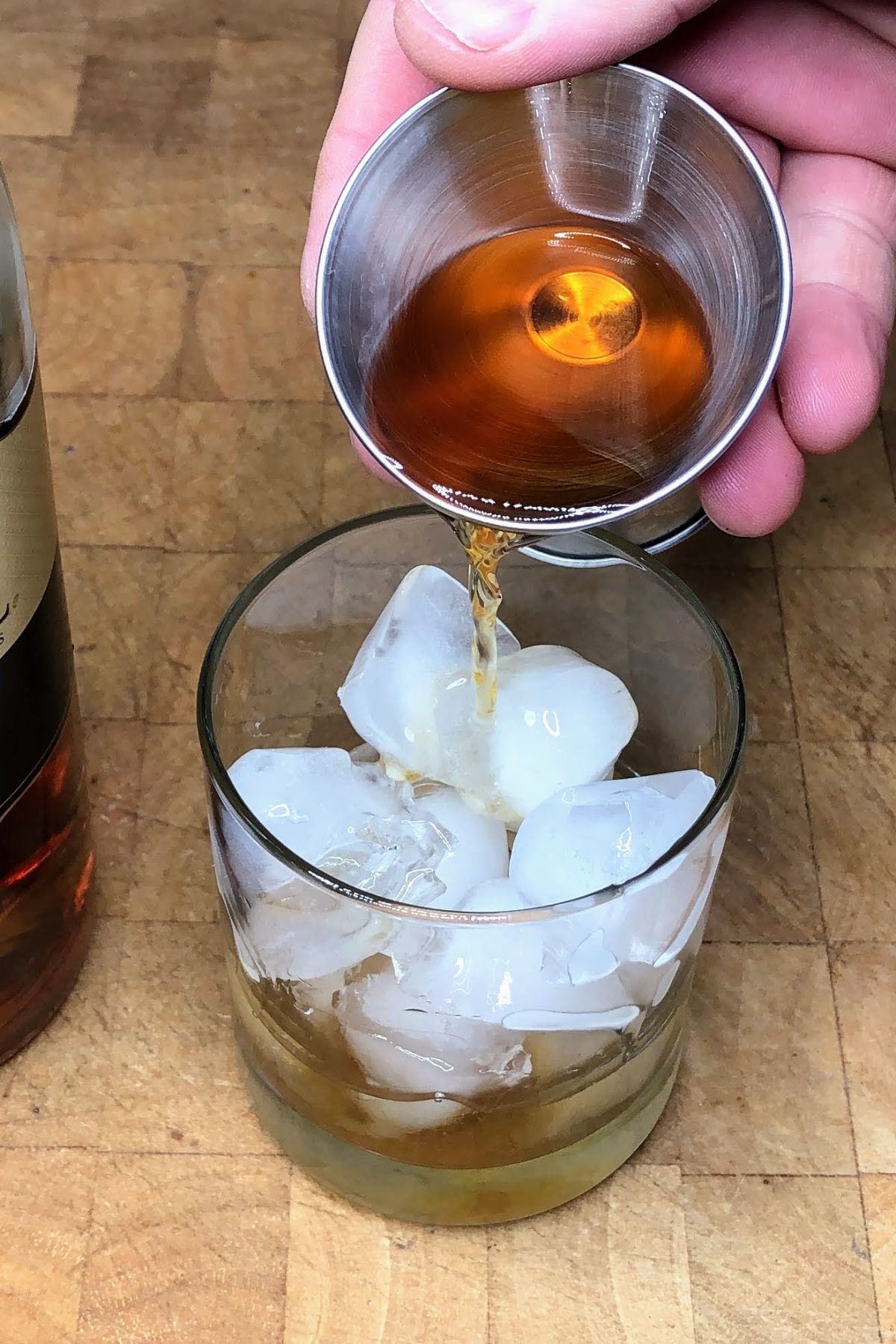 Pouring brandy from a jigger into a glass.