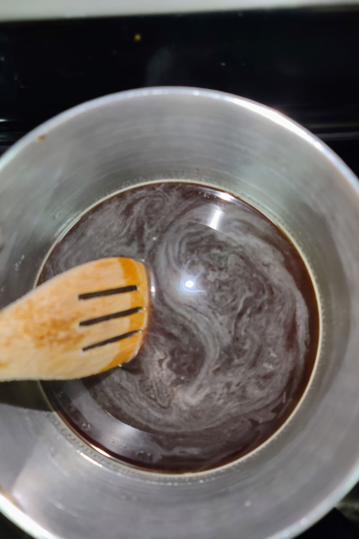 Stirring brown sugar syrup in a pot on the stove.