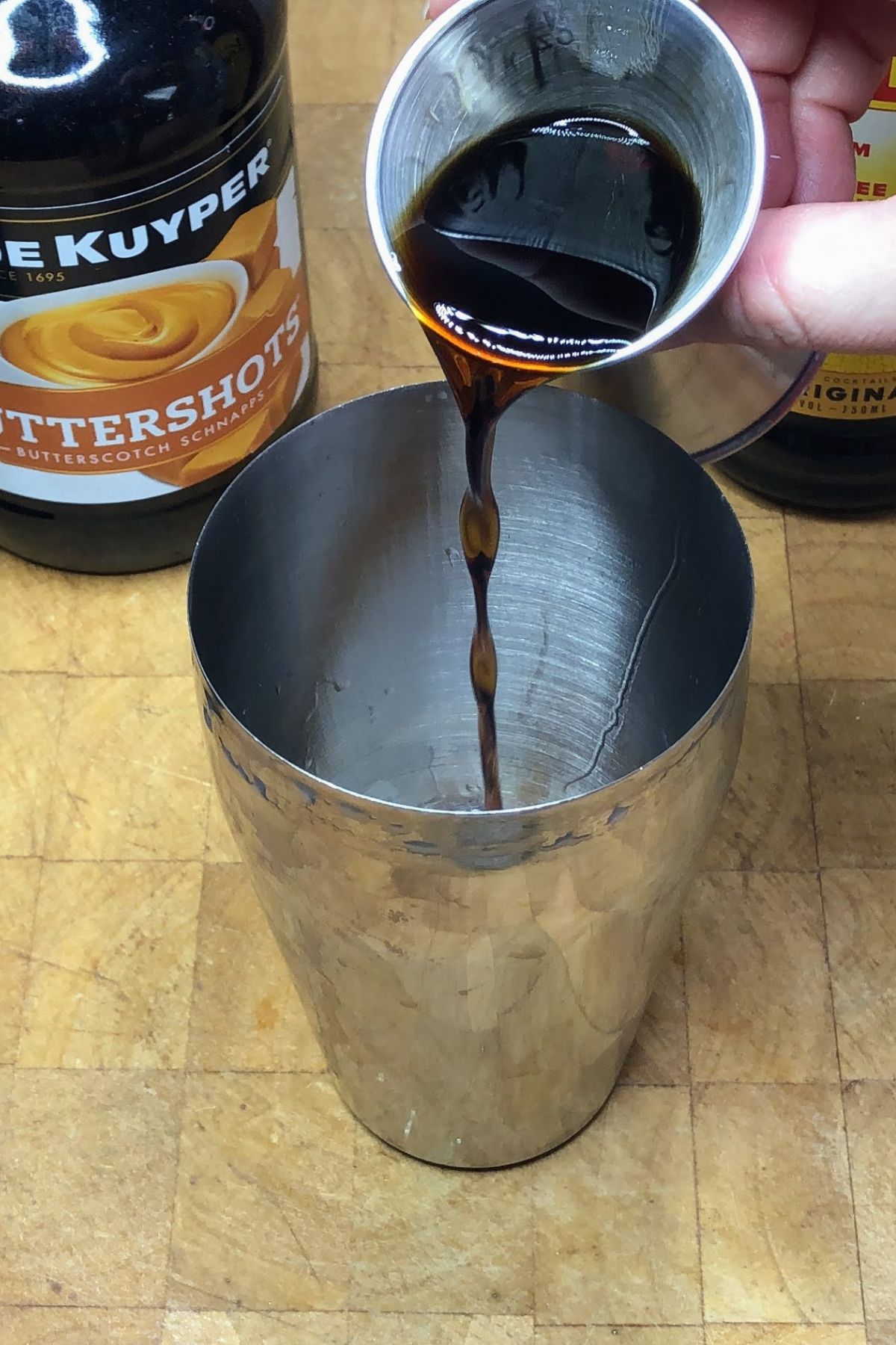 Pouring kahlua from jigger into the shaker.