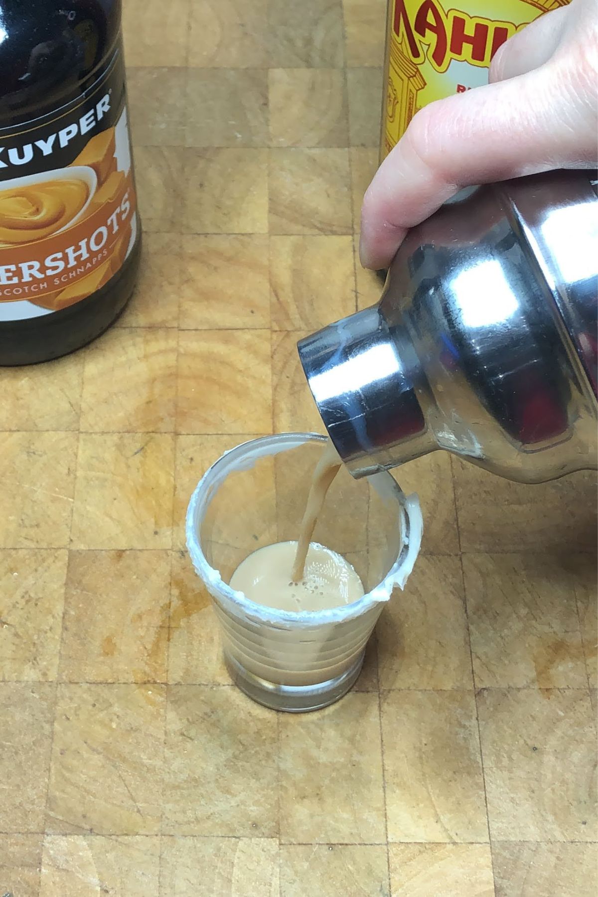 Pouring carrot cake shot from a shaker into a shot glass.