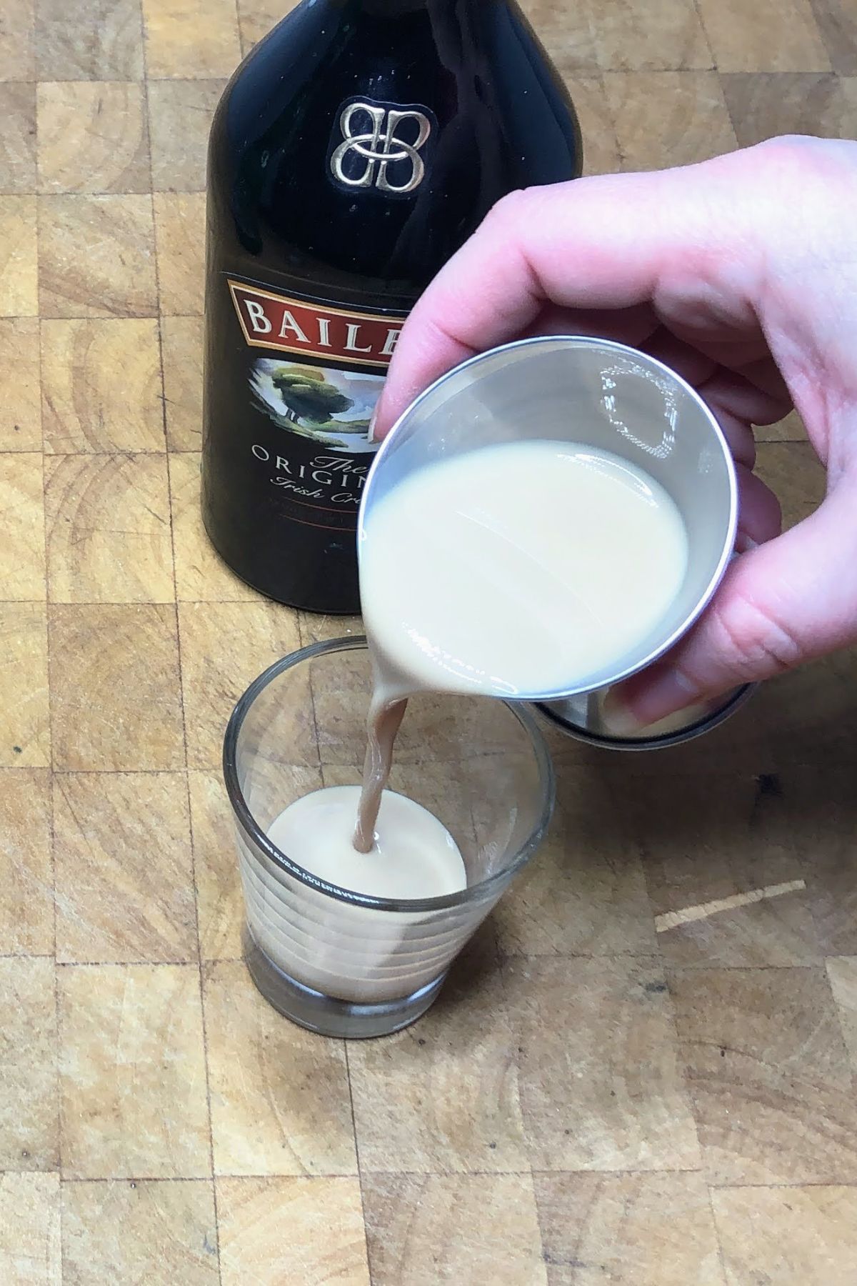 Pouring irish cream from jigger into the shot glass.