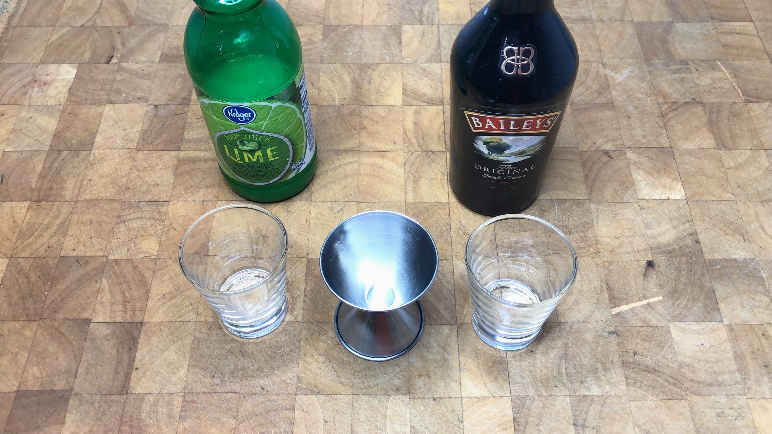 Lime juice and irish cream next to a jigger and two shot glasses.