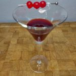 Cherry martini with three cherries in the glass on a wooden table.