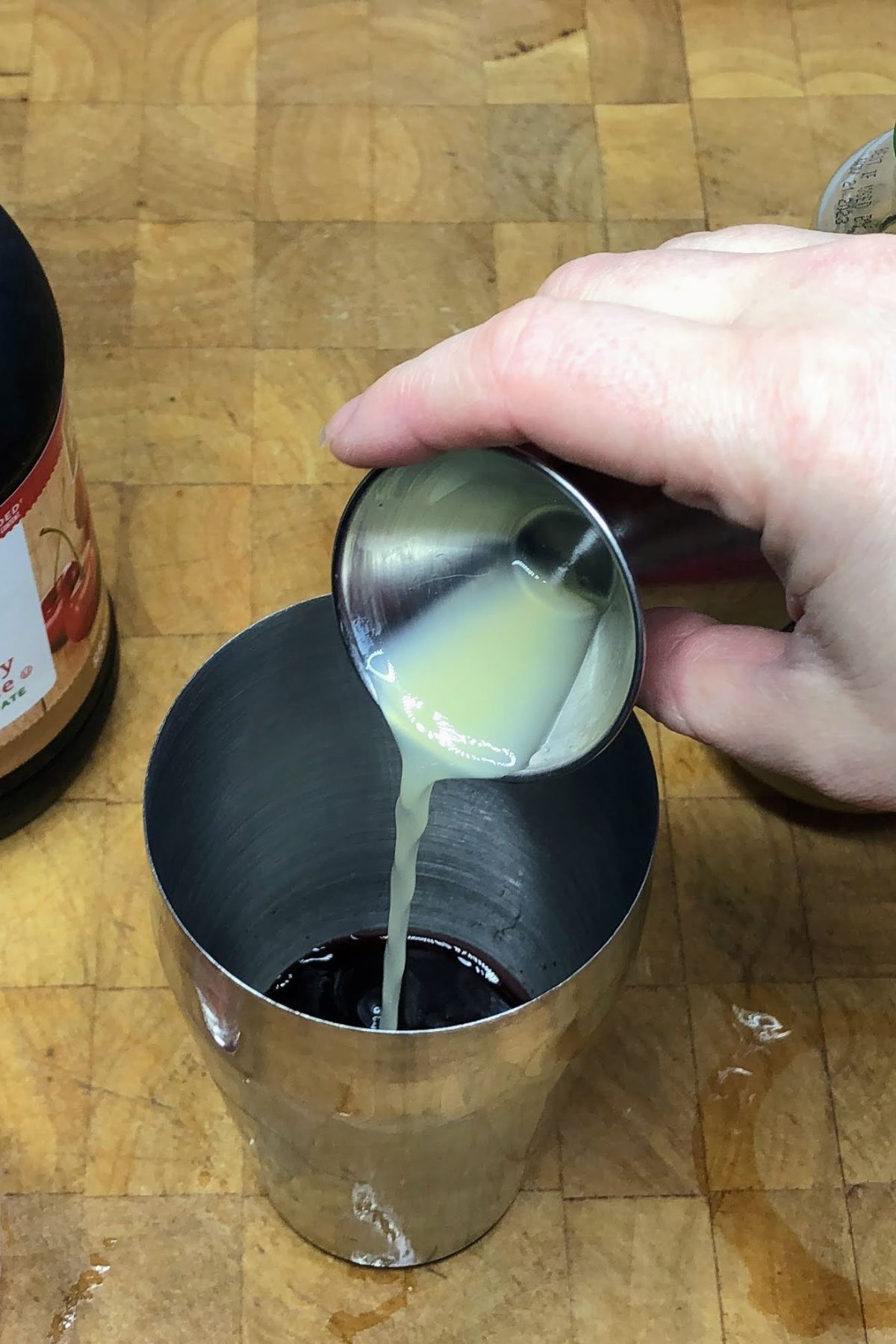 Pouring lemon juice from jigger into the cocktail shaker.
