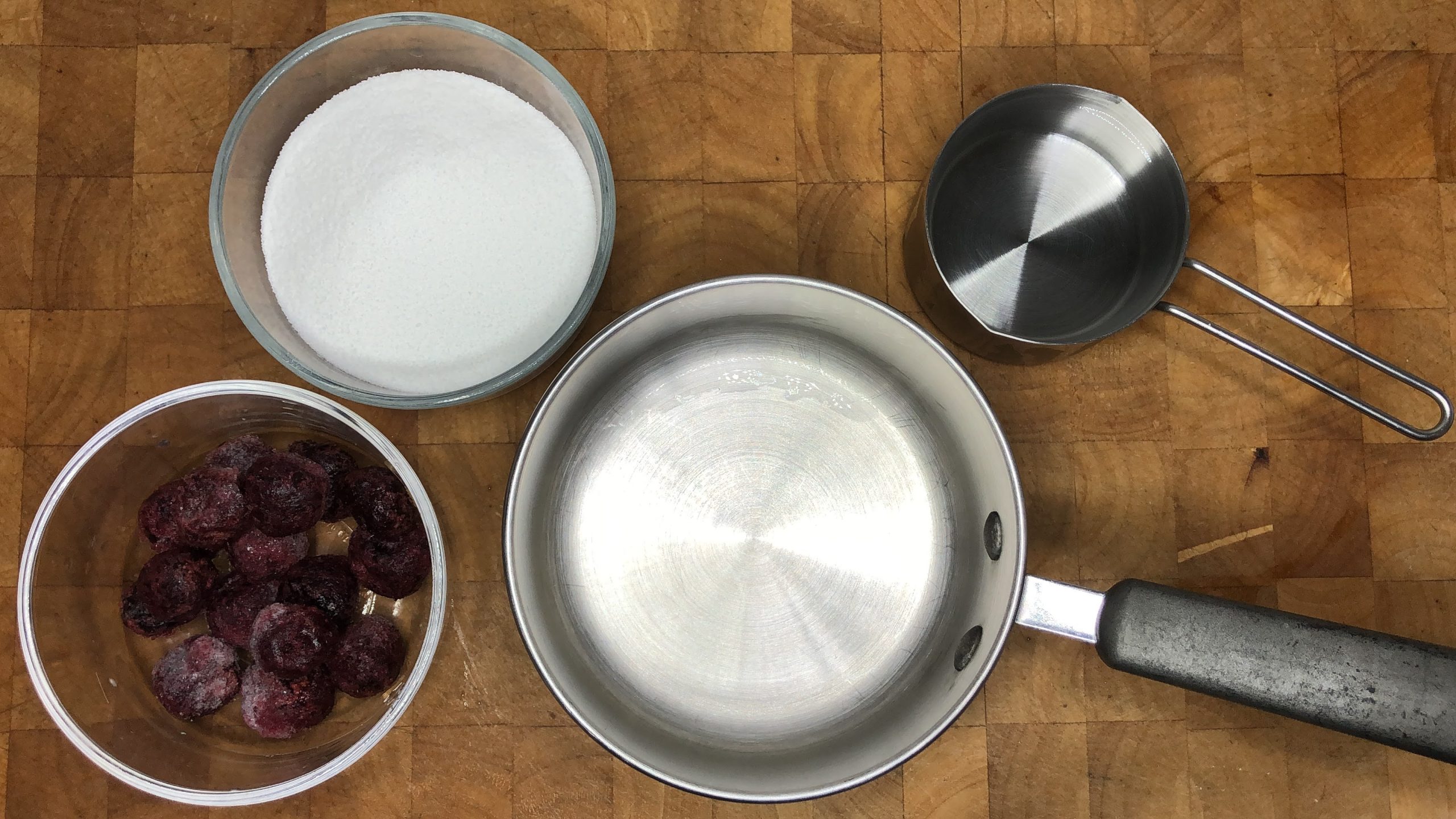 Empty pot next to bowls of cherries, sugar and water.