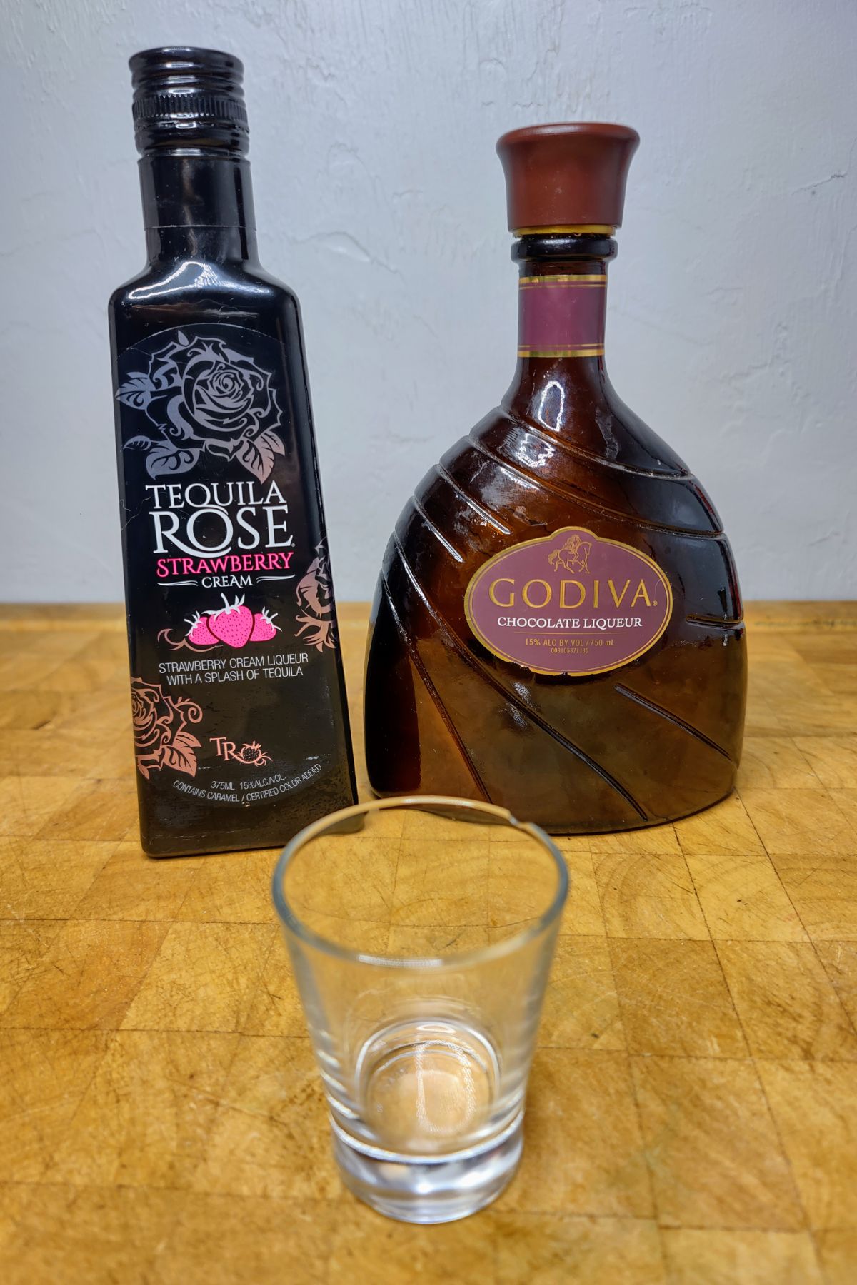 Bottle of tequila rose and godiva behind a shot glass.