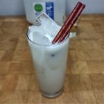 Cinnamon milk in a highball glass with a cinnamon stick on the glass and ingredients in the background.
