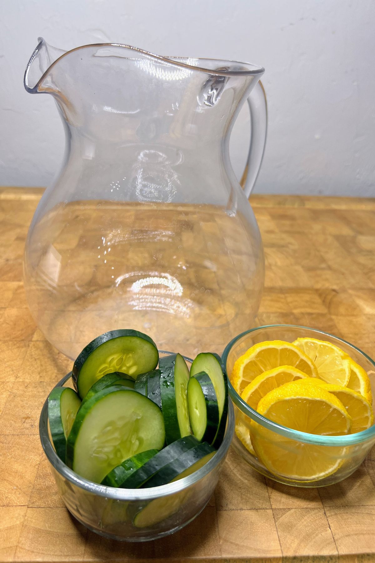 Pitcher behind bowls of sliced cucumber and lemons.