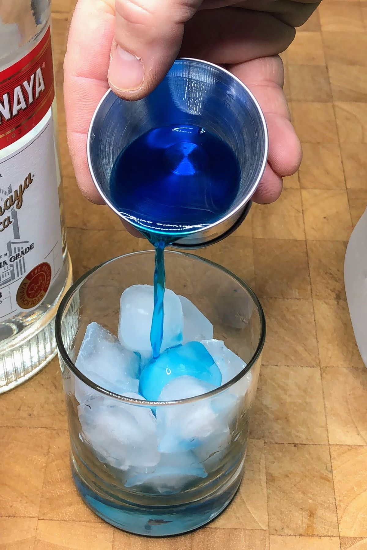 Pouring blue curacao into a rocks glass.