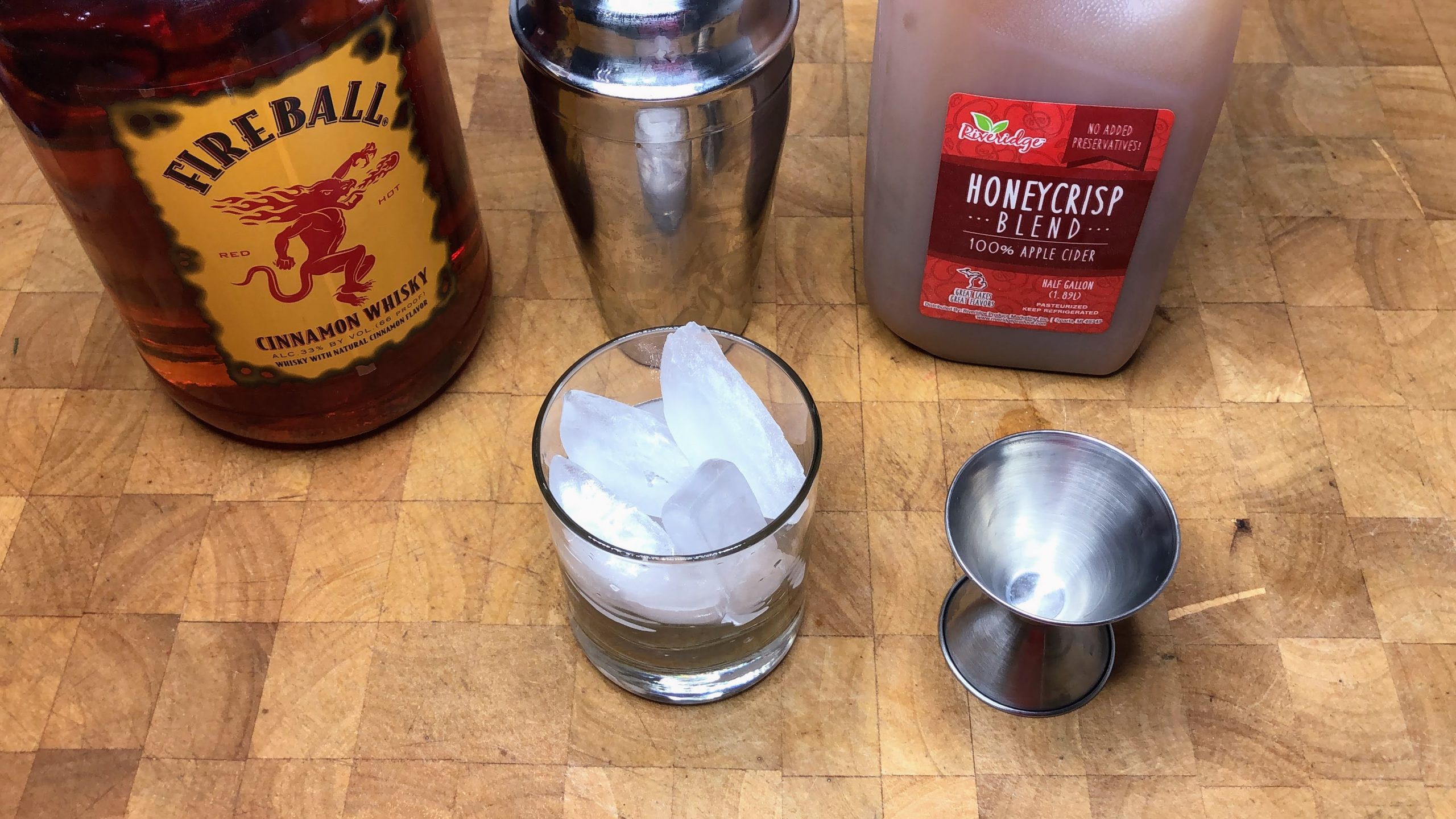 Fireball next to shaker, apple cider, rocks glass with ice and jigger.