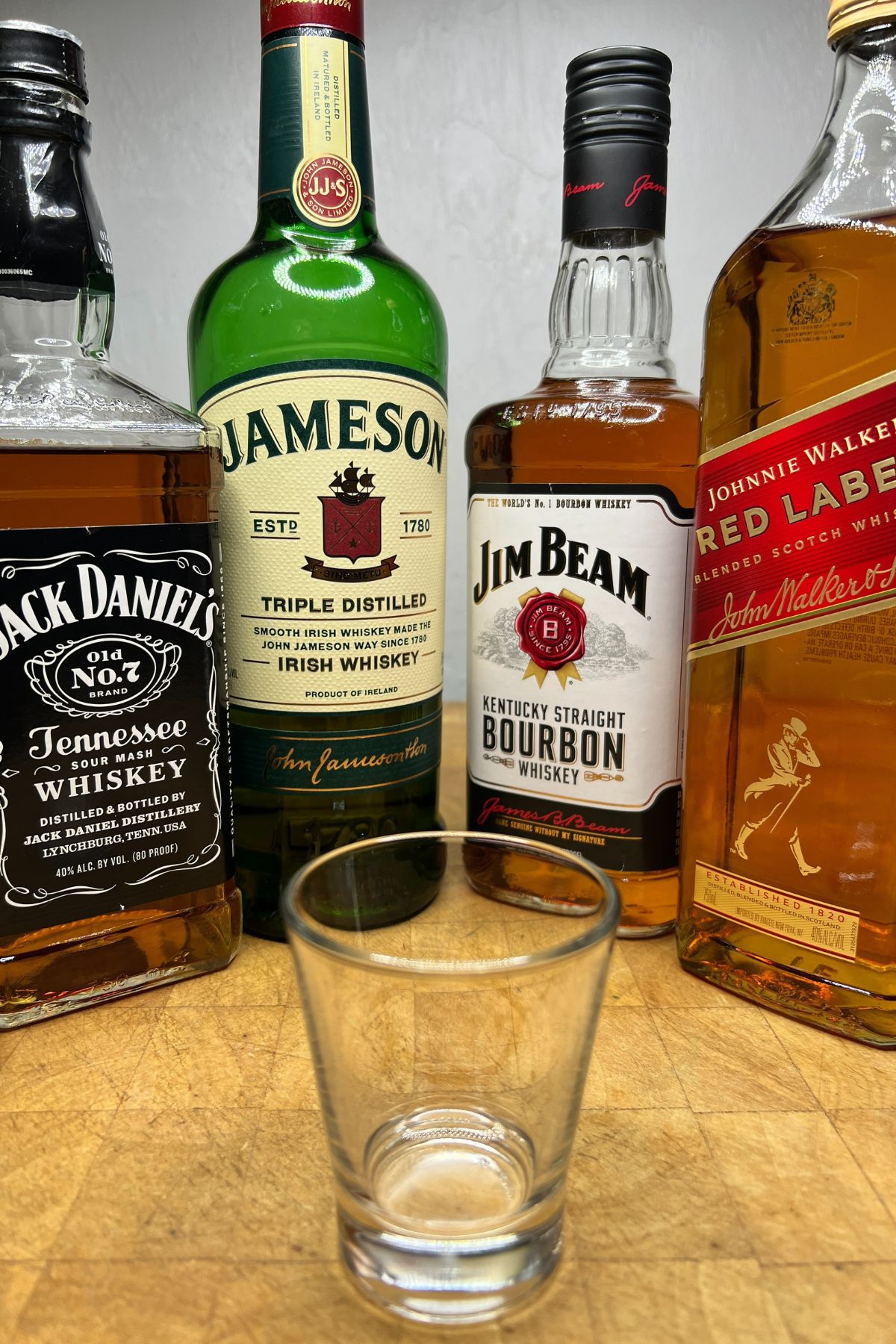 Bottles of Jack Daniels, Jamesons, Jim Beam and Johnnie Walker behind a shot glass.