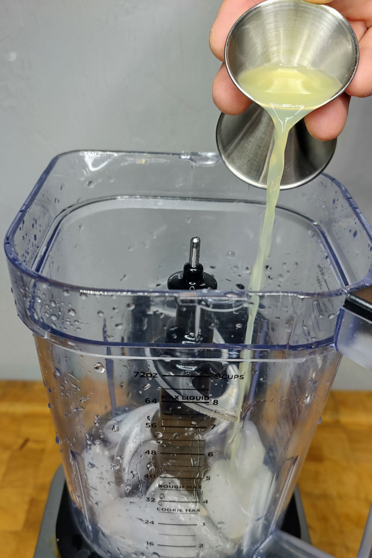 Pouring lime juice from a jigger into a blender.