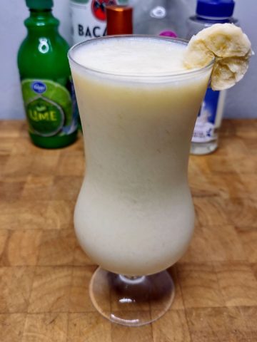 Frozen banana daquiri on a wooden table with ingredients in the background.
