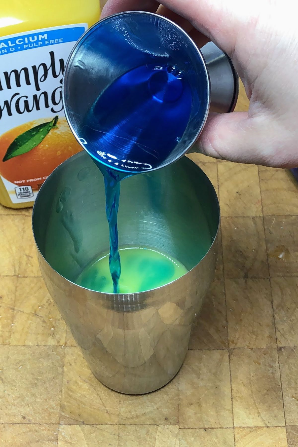 Pouring blue curacao from jigger into shaker.