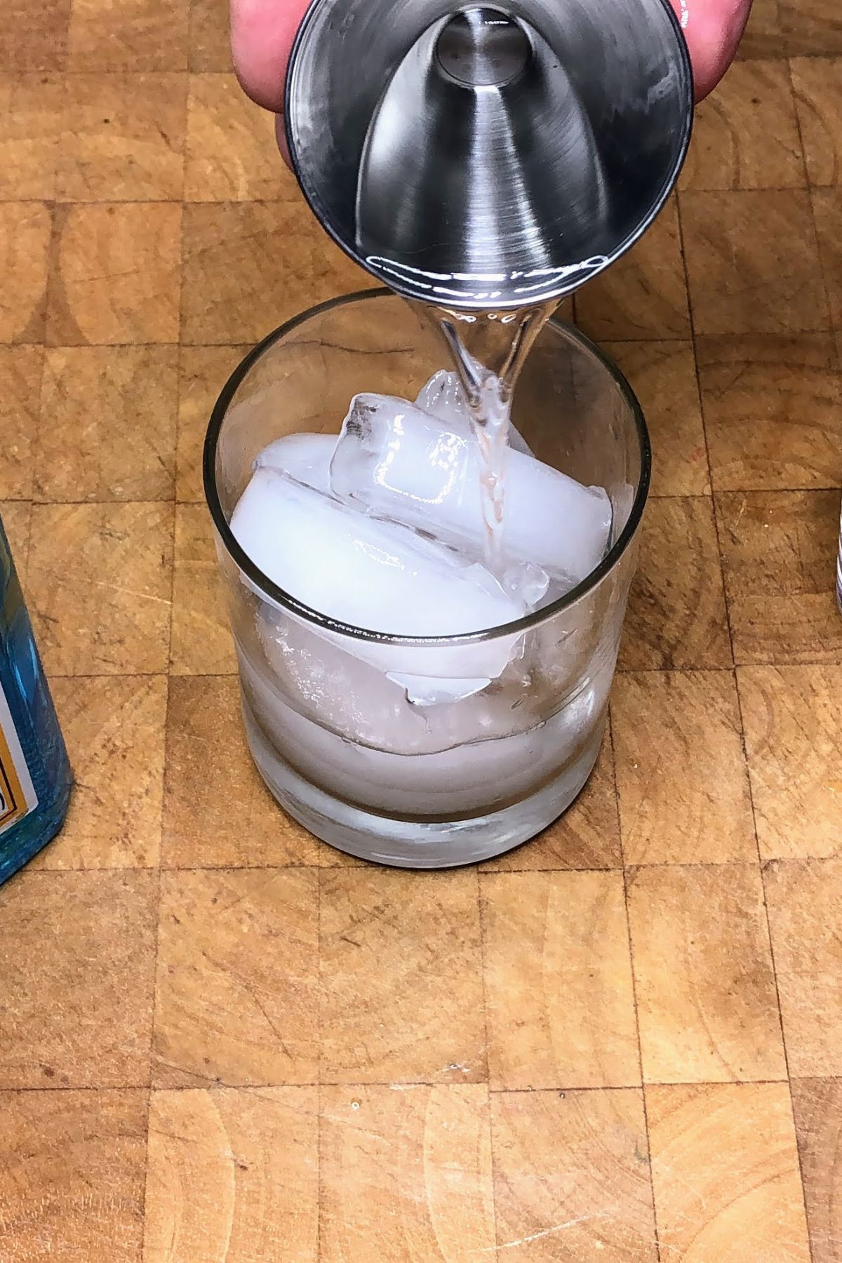 Pouring gin from a jigger into a rocks glass.