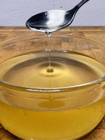 Ginger simple syrup in a bowl being scooped by a bowl.