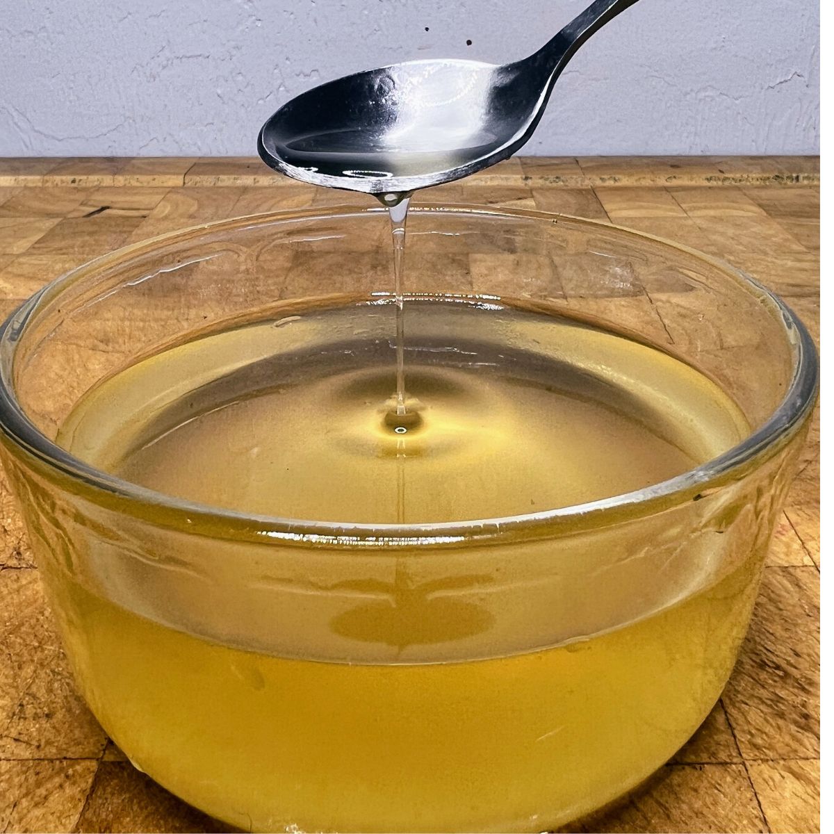 Ginger simple syrup in a bowl being scooped by a bowl.
