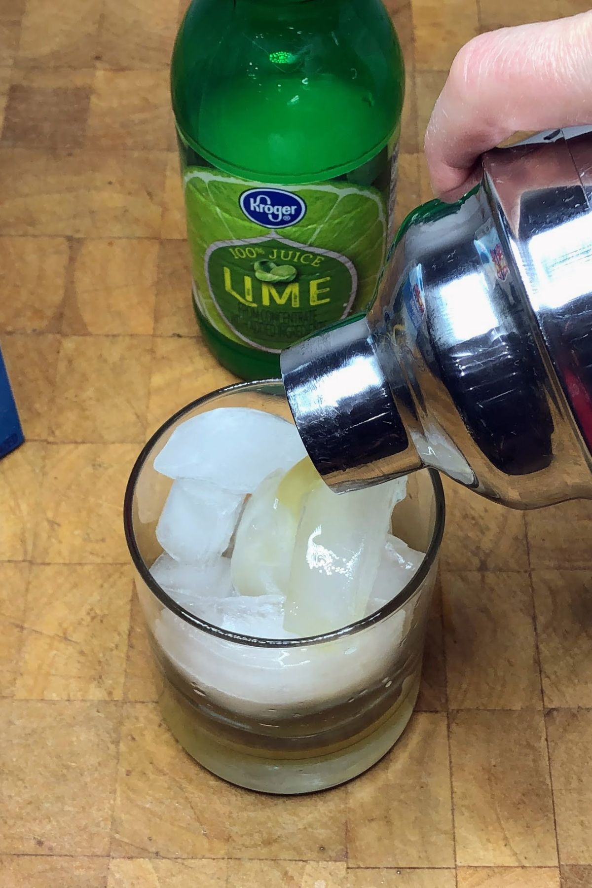 Pouring ginger beer mocktail from a shaker into a rocks glass.
