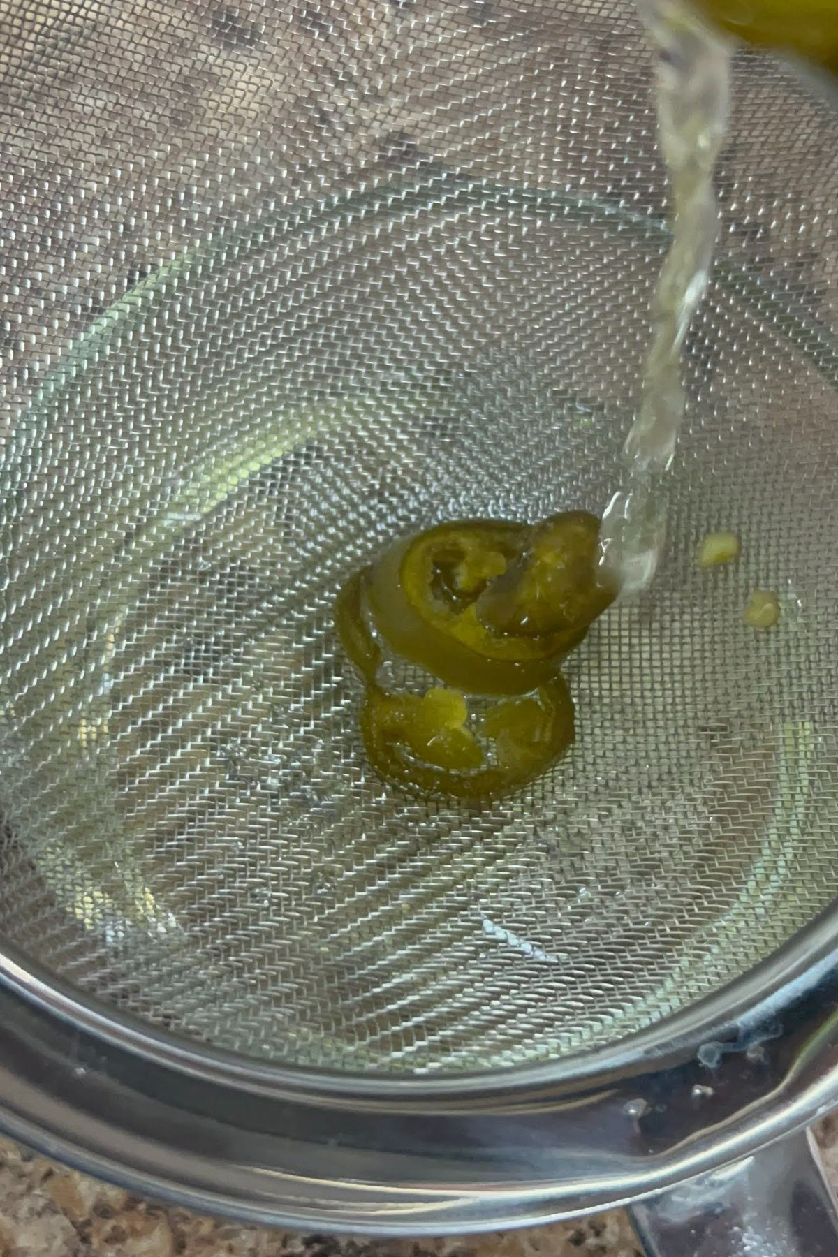 Pouring jalapeno syrup into a strainer.