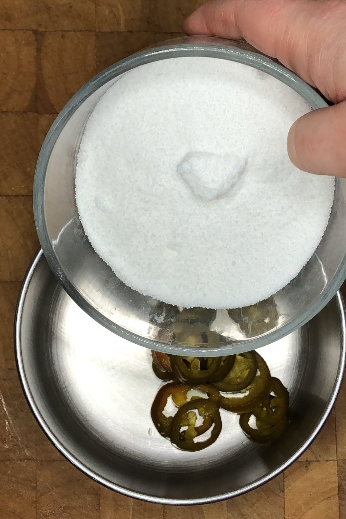 Pouring sugar into a pot with jalapeno slices