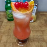 Mai tai mocktail with cherries and orange on top of the glass and ingredients in the background.