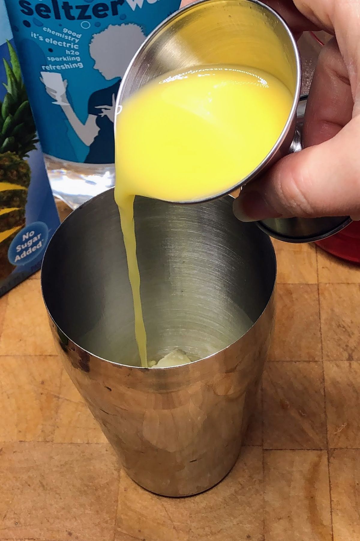 Pouring orange juice from a jigger into a cocktail shaker.