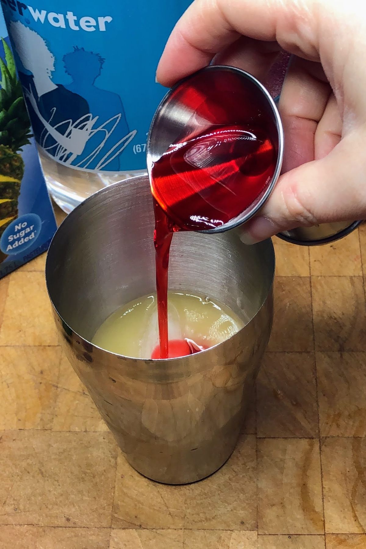 Pouring grenadine from a jigger into a cocktail shaker.