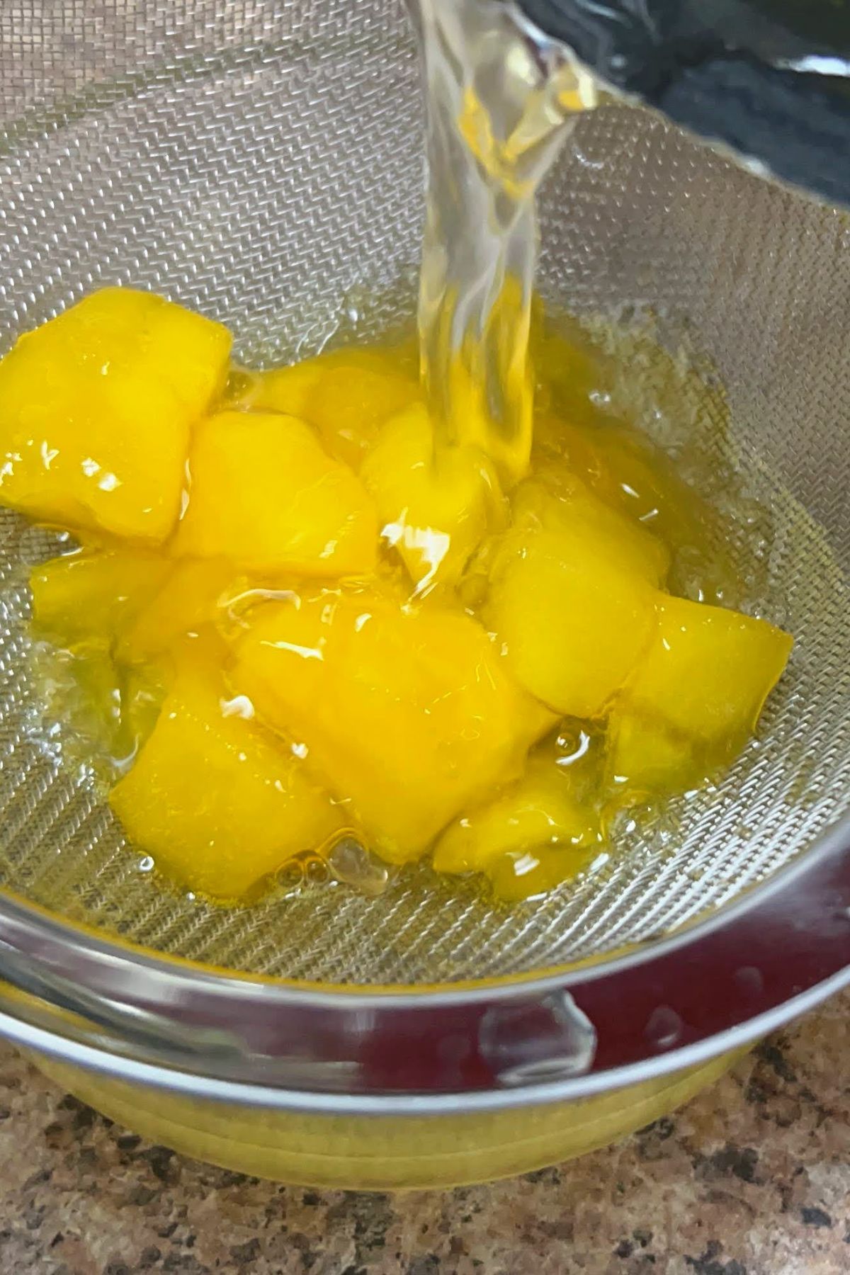 Pouring mango syrup from a pot into a strainer.