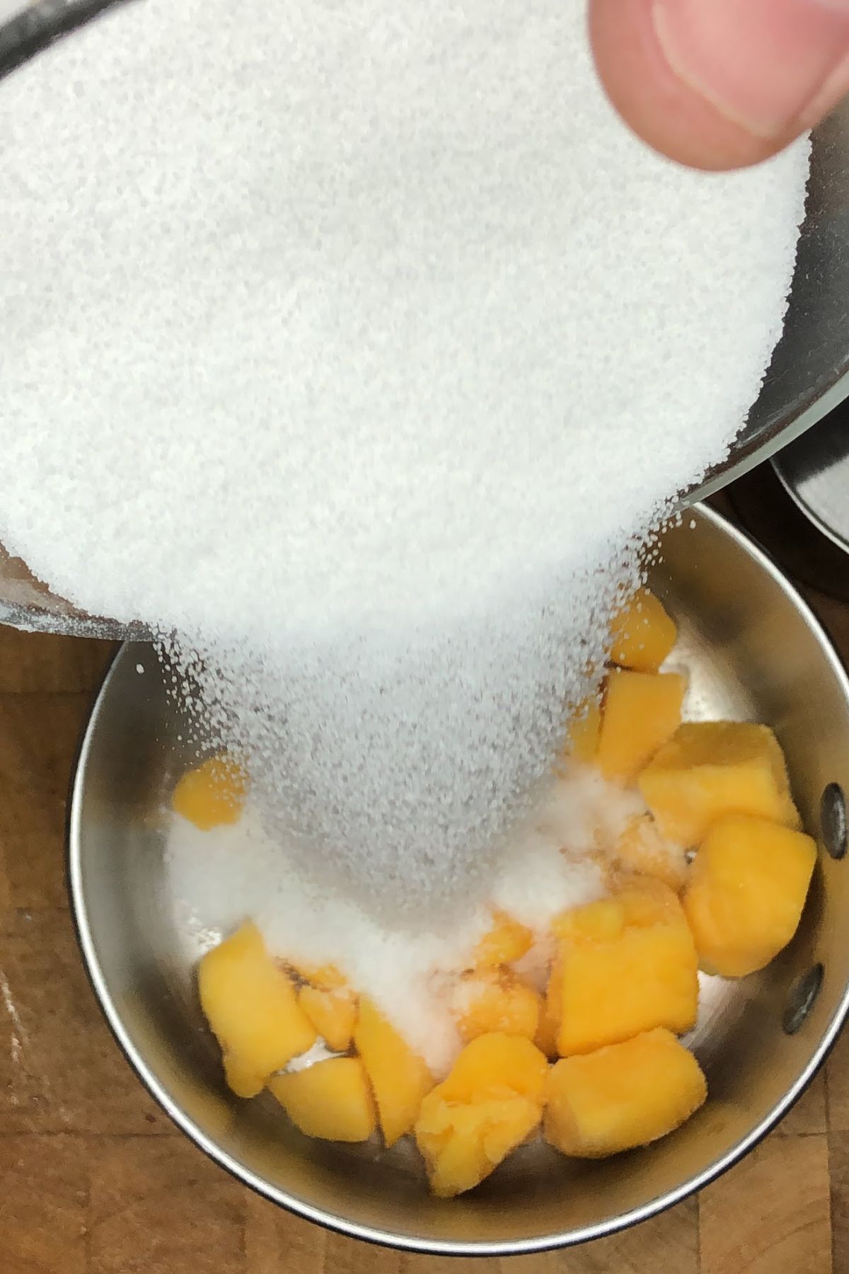 Pouring sugar into a pot with mango.