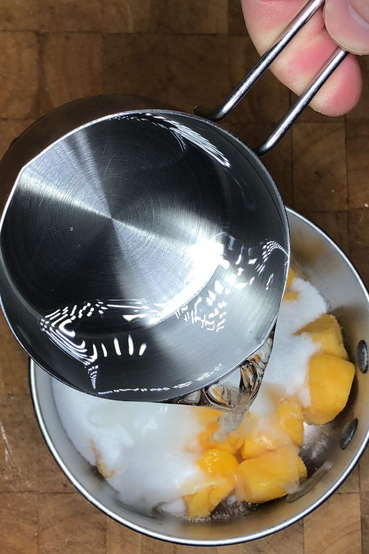 Pouring water into a pot with sugar and mango.