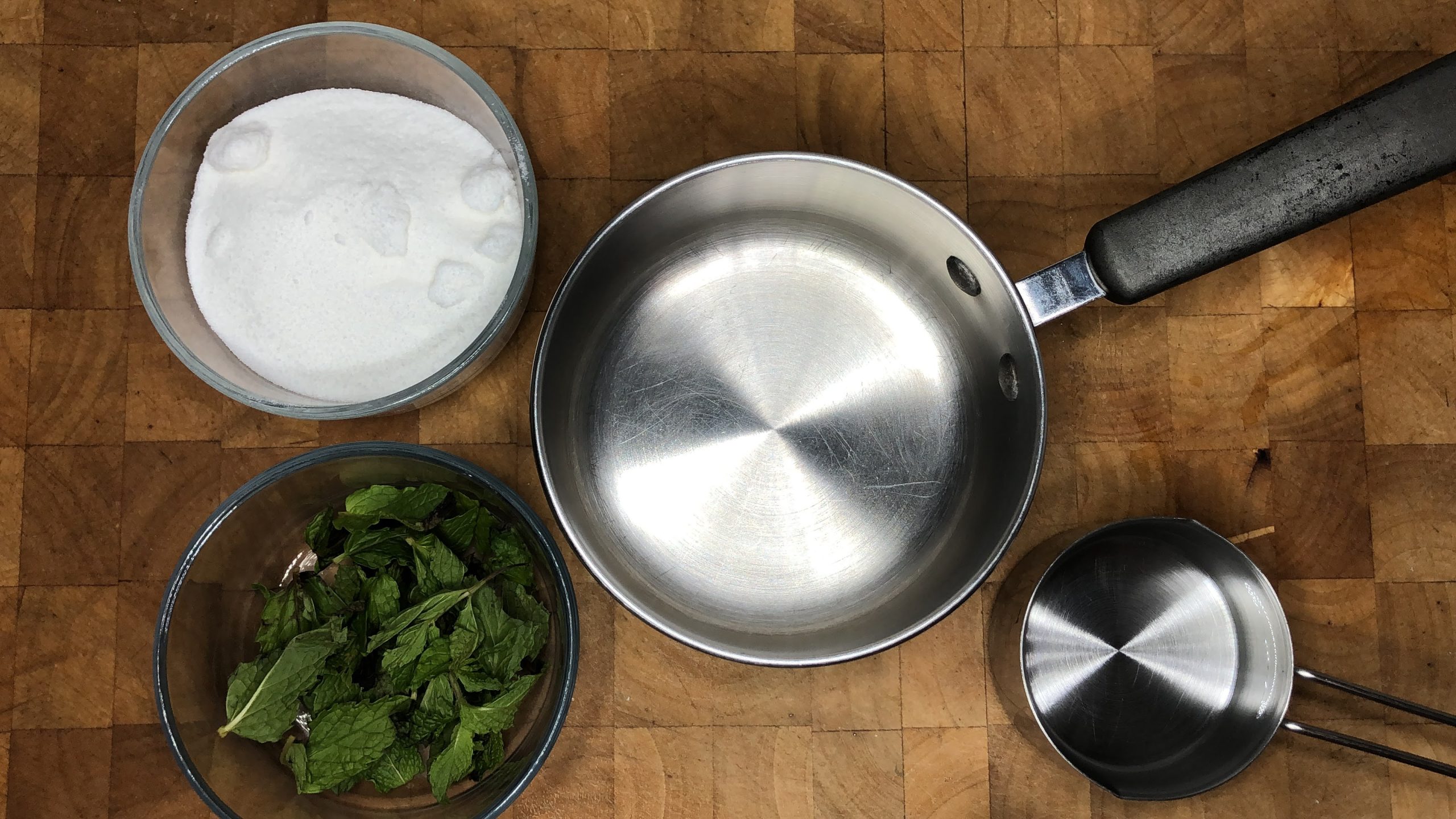 An empty pot next to bowls of sugar, water and mint leaves.