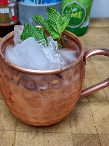 Moscow mule mocktail on a wooden table with ingredients in the background.