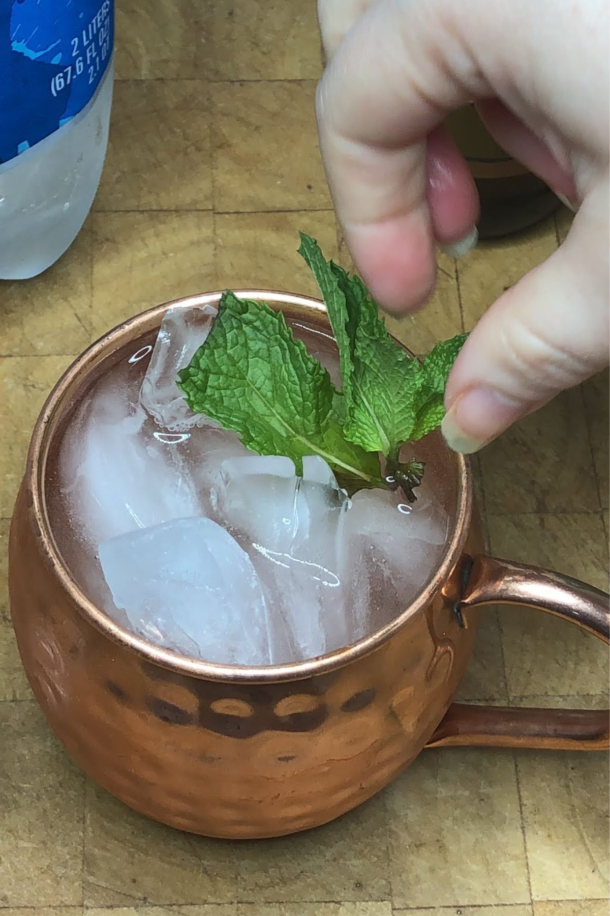Adding mint leaves to the top of a drink that is in a copper mug.