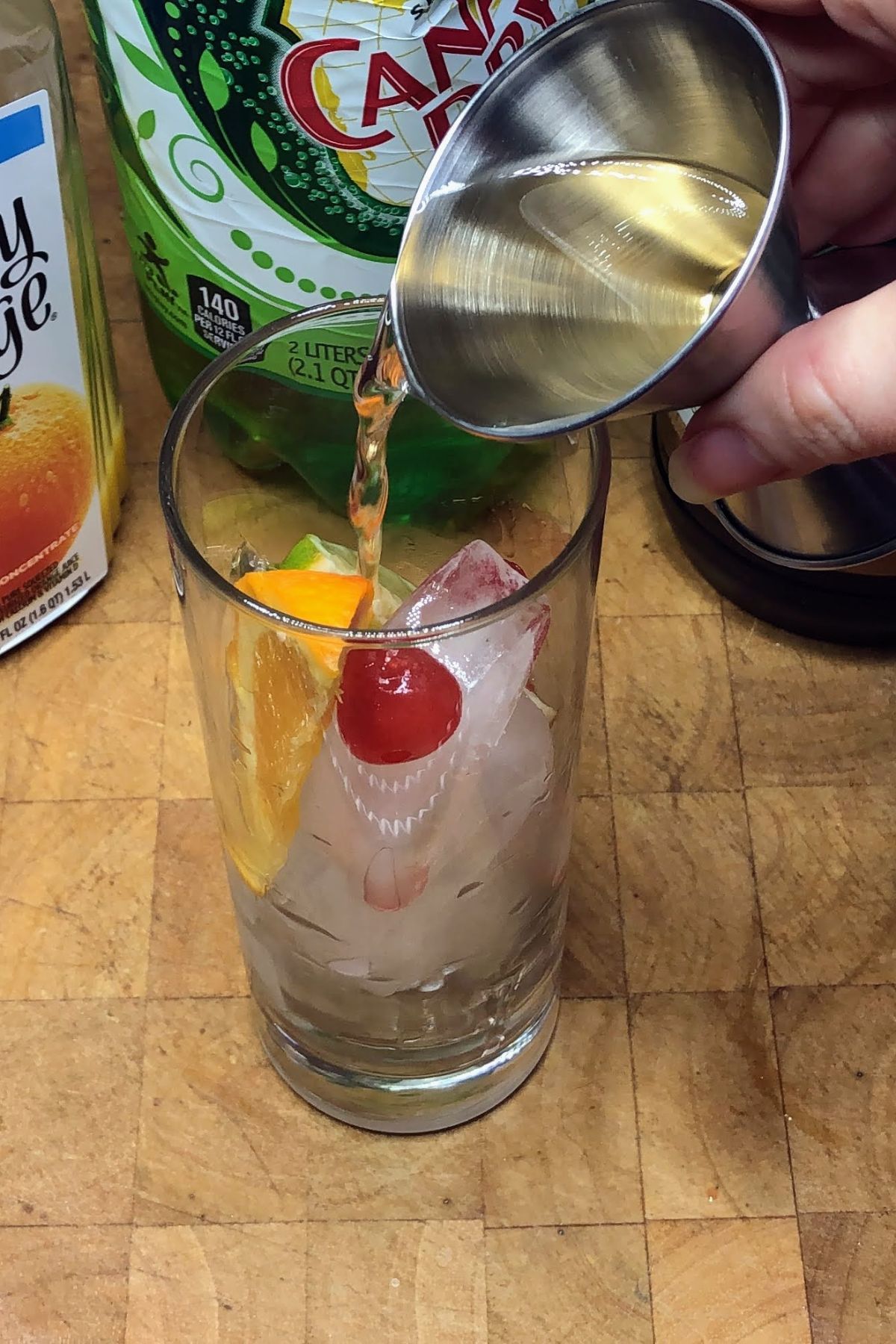 Pouring ginger ale from a jigger into a highball glass.