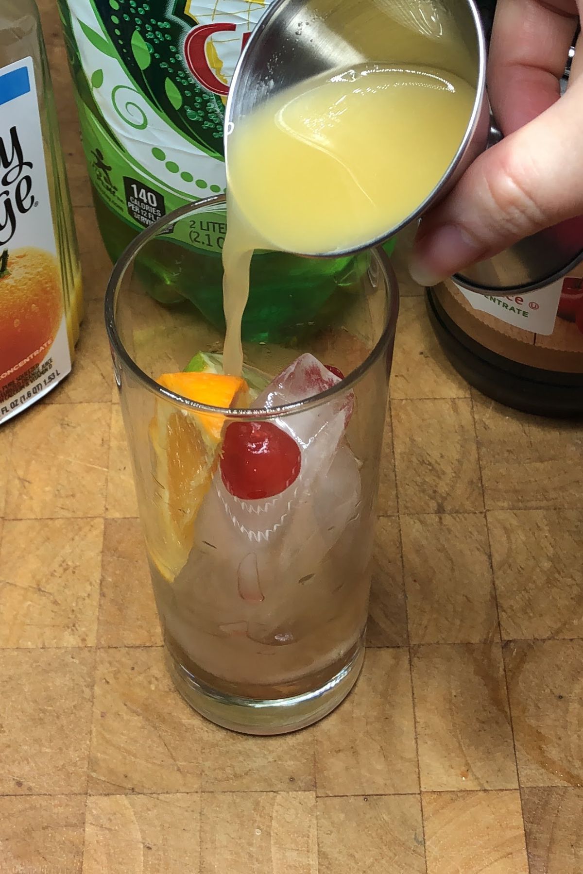 Pouring pineapple juice from a jigger into a highball glass.